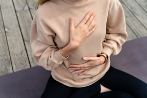 Frau sitzt im Schneidersitz mit Hand auf Brust und Bauch beim Atemtraining zur Meditation und Entspannung