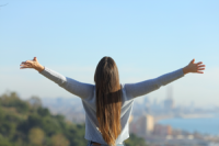 Frau mit offenen Armen vor blauem Himmel